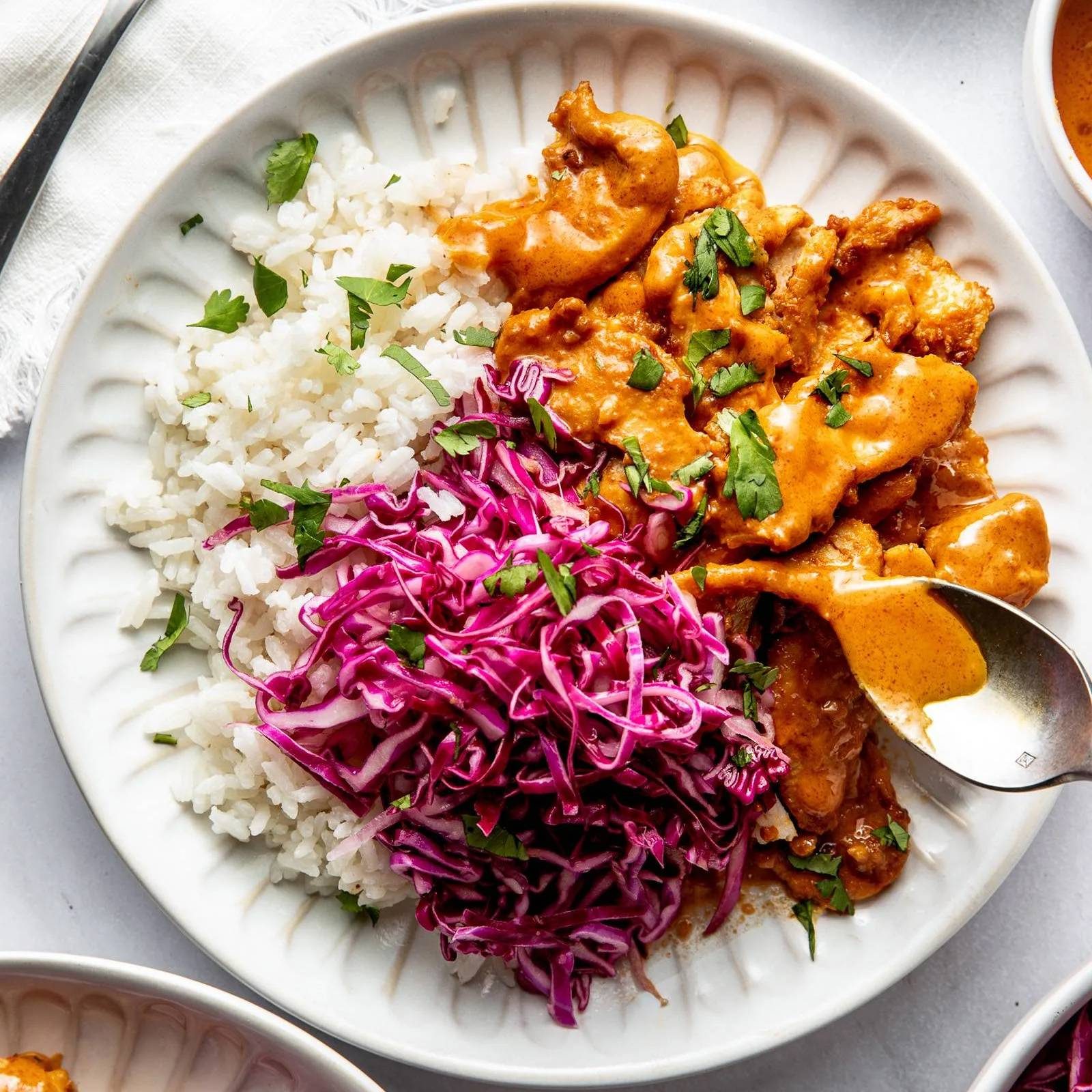 Peanut chicken on a plate with rice and slaw.