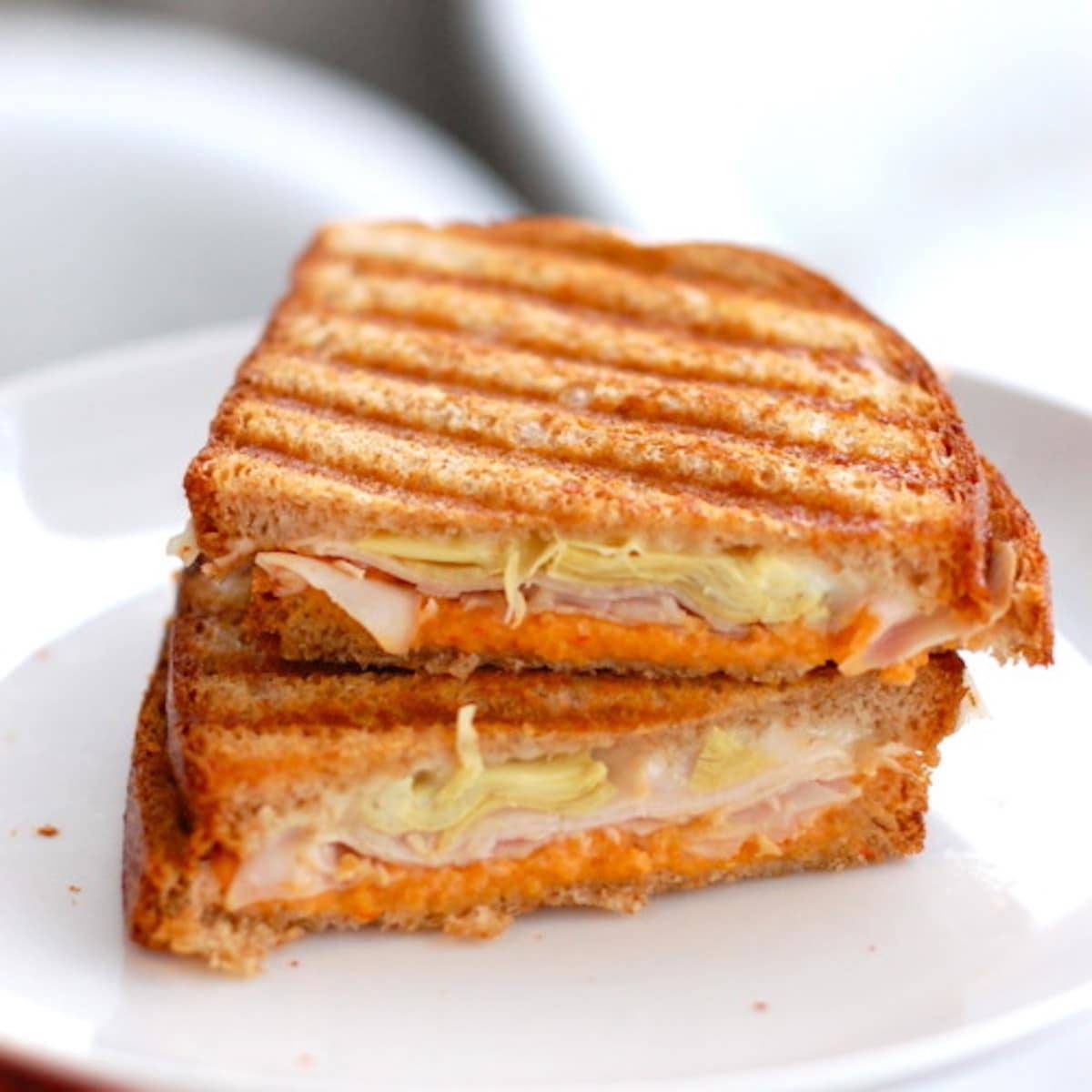 Red pepper and artichoke panini sliced in half on a white plate.